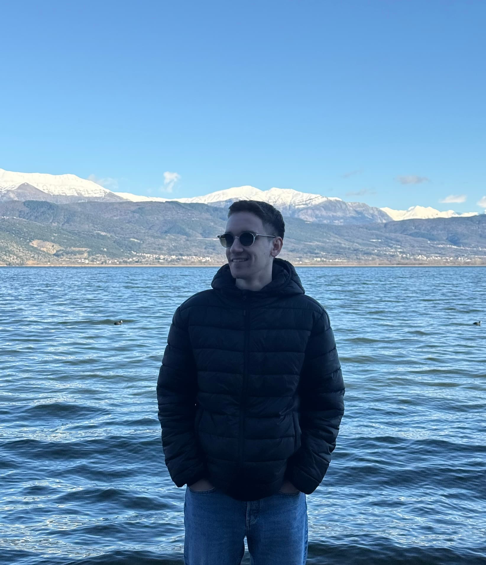 Christos Kechagias wearing sunglasses beside a lake with snow-covered mountains
